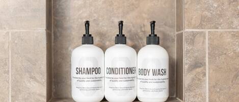 Three white bottles of shampoo, conditioner, and body wash in a tiled shelf.