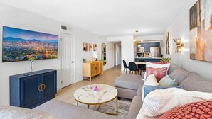 A modern living room with a large TV, a sofa, a coffee table, and a dining area with chairs and a table. - Maya Motel (Scottsdale)
