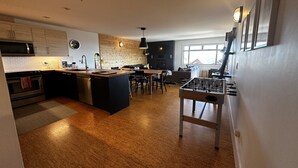 A modern kitchen with a central island, wooden flooring, and a foosball table.