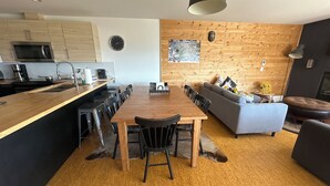 A modern kitchen with a wooden countertop, a dining table with chairs, a sofa, and a fireplace.