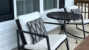 Une véranda avec deux chaises et une petite table, un revêtement extérieur blanc et de grandes fenêtres.