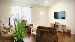 Un salon avec un ventilateur de plafond, un téléviseur fixé au mur, un canapé, un fauteuil et une table basse.