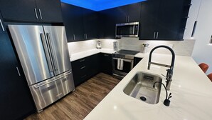 Una cocina moderna con armarios oscuros, electrodomésticos de acero inoxidable y encimera blanca.