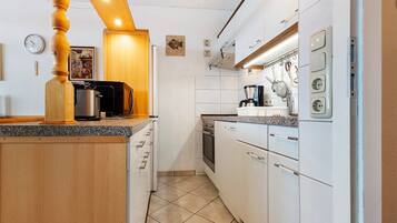 Une cuisine compacte avec des meubles blancs, un îlot central en bois, un four encastré et une machine à café.