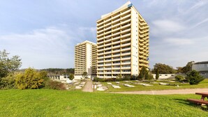 Un immeuble de grande hauteur doté de nombreux balcons, entouré d’une zone verdoyante bien entretenue et d’un cimetière.
