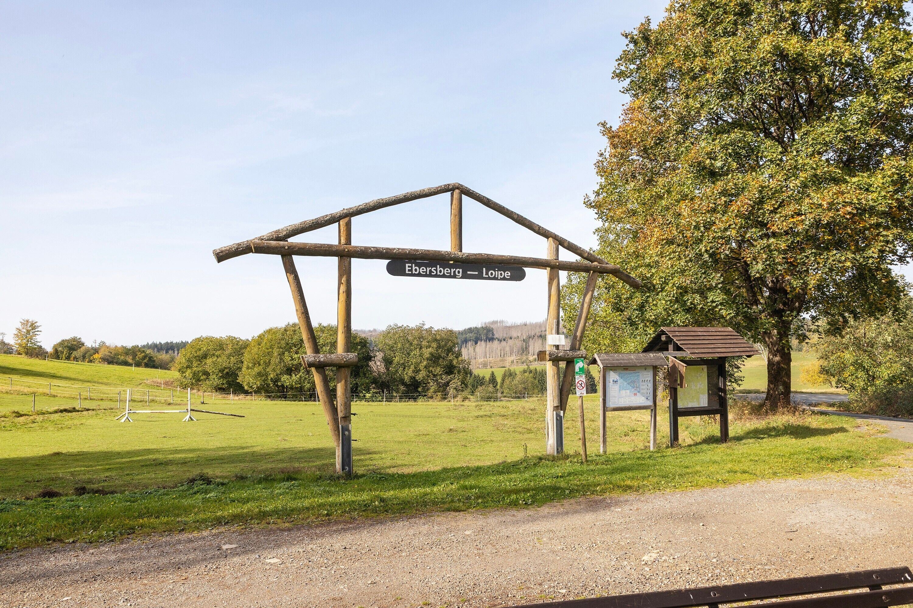A rural signpost with 'Ebersberg - Loipe' written on it, a gravel path, and a bench.