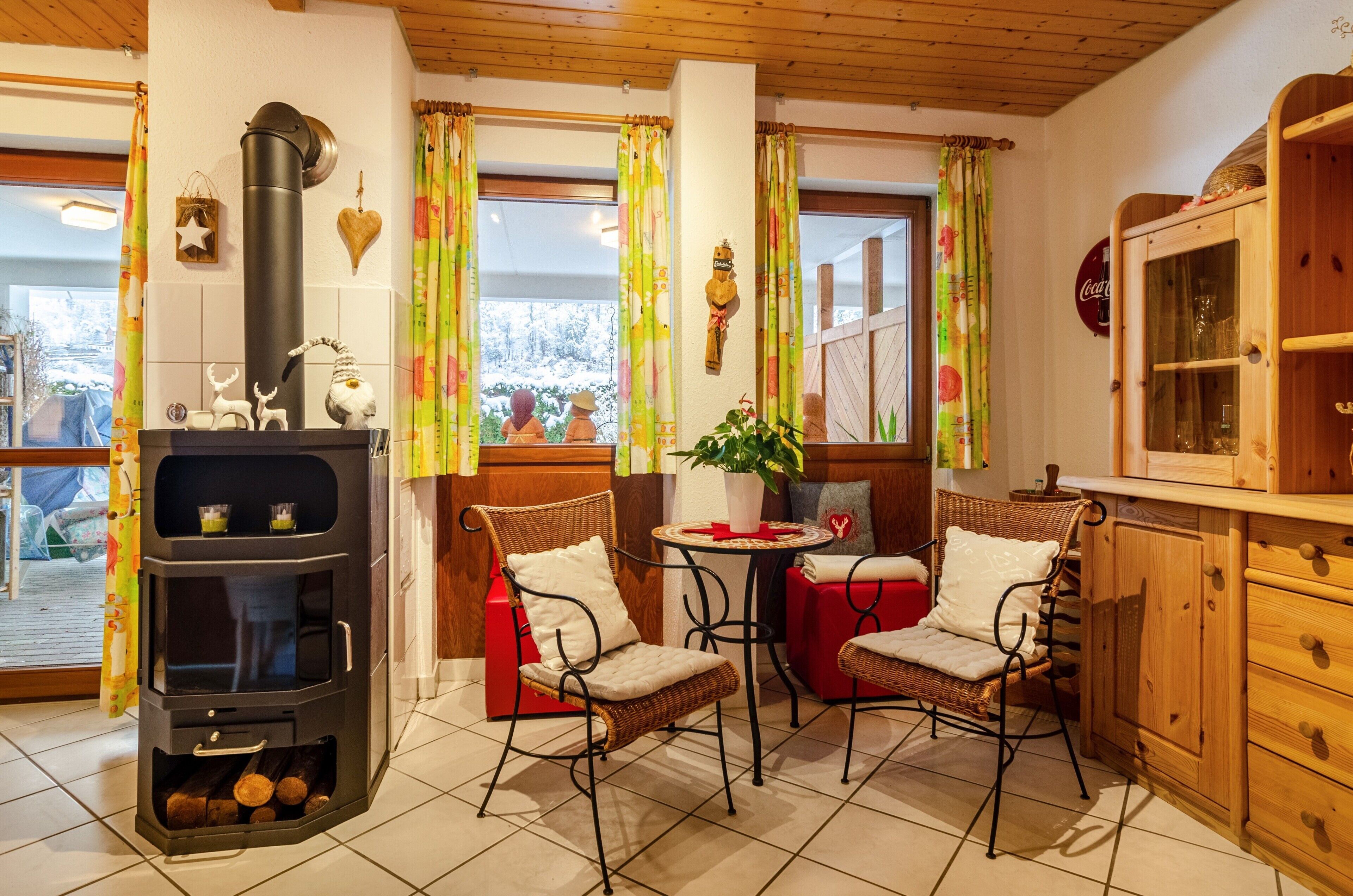 Une cuisine chaleureuse avec un poêle à bois, des chaises en osier, une petite table et des meubles de rangement en bois.
