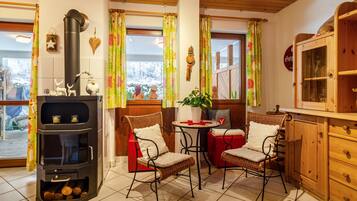 Une cuisine chaleureuse avec un poêle à bois, des chaises en osier, une petite table et des meubles de rangement en bois.