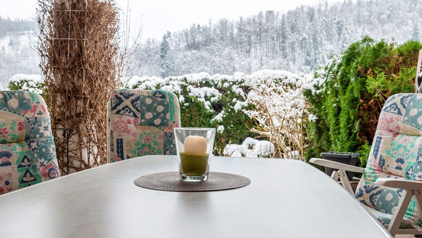 Una mesa de comedor con una taza de té, sillas con diseños y vista a un paisaje nevado.