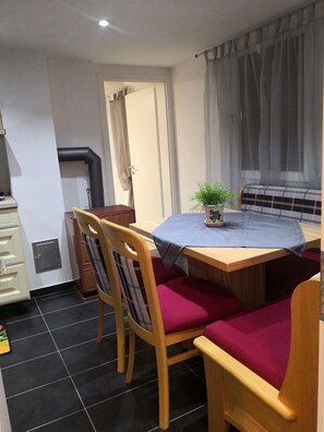A compact room with a dining table, chairs, a small potted plant, a bench, and a window with curtains.