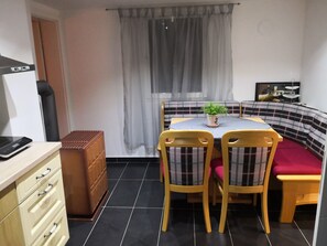 Een kleine woonruimte met een kitchenette, een eethoek met tafel en stoelen, een bank en een raam met gordijnen.
