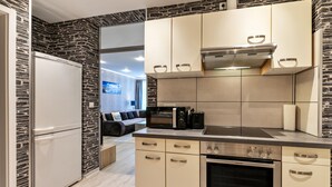 Une cuisine moderne équipée d’un four encastré, d’un four à micro-ondes et d’une cuisinière. Un mur en pierre se trouve sur un côté, et le sol est en bois.