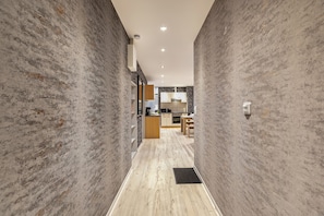 A hallway with textured walls and a wooden floor leading to a kitchen area with modern appliances and cabinetry.