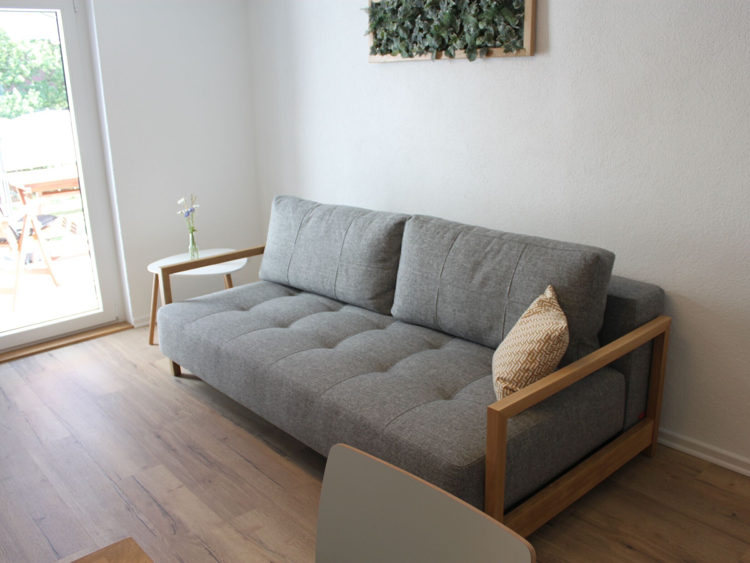 A modern living room with a grey sofa, a small side table, and a wooden floor.