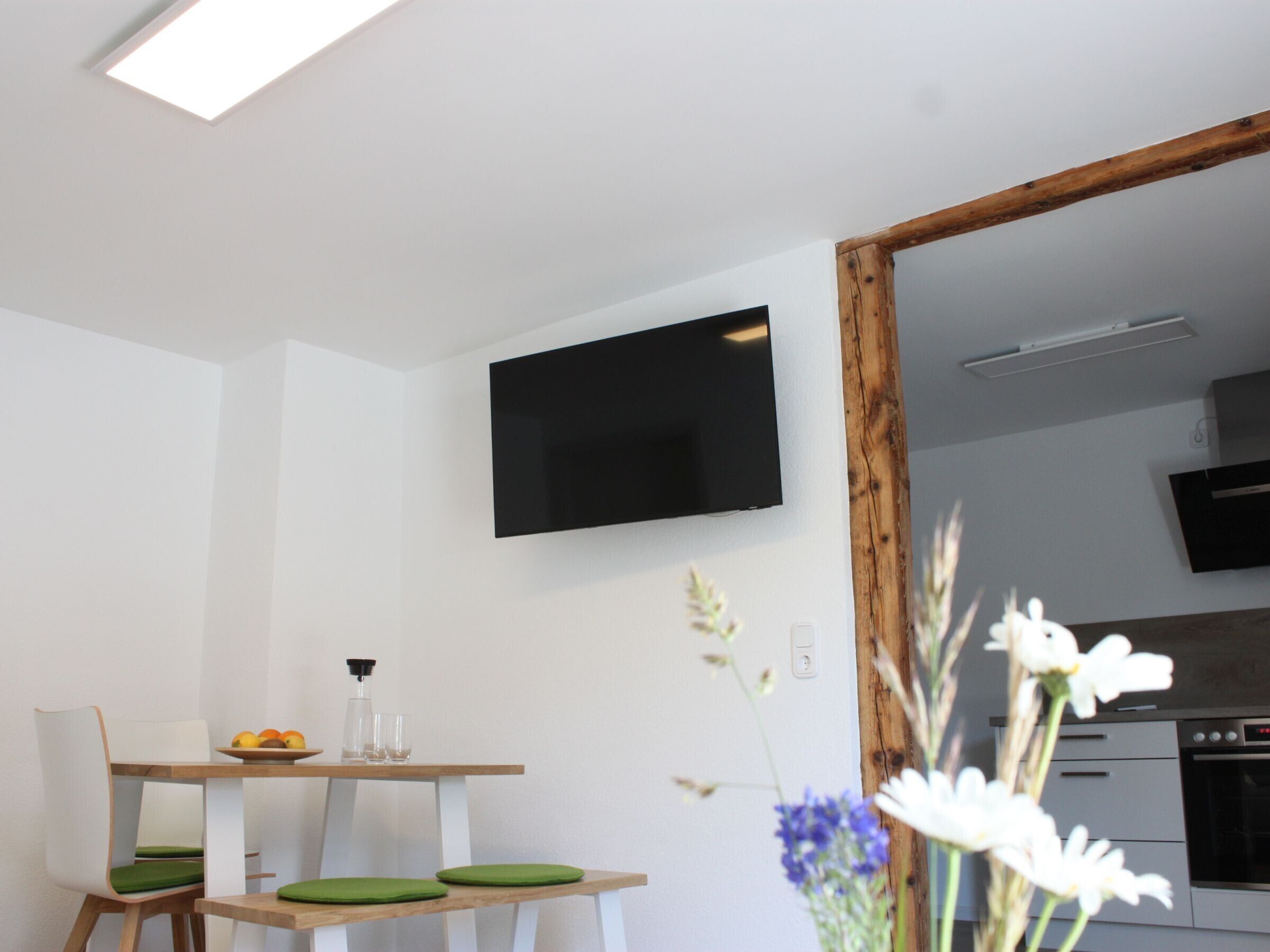 A modern kitchen with a flat-screen TV, wooden cabinets, and a dining area with a table and chairs.