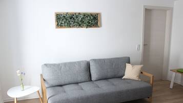 A grey sofa with wooden legs, a small white side table, and a vase with flowers.