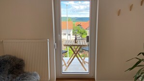 Une pièce avec une porte donnant sur un espace extérieur, un radiateur, un fauteuil en fourrure et une petite table avec une bouteille.