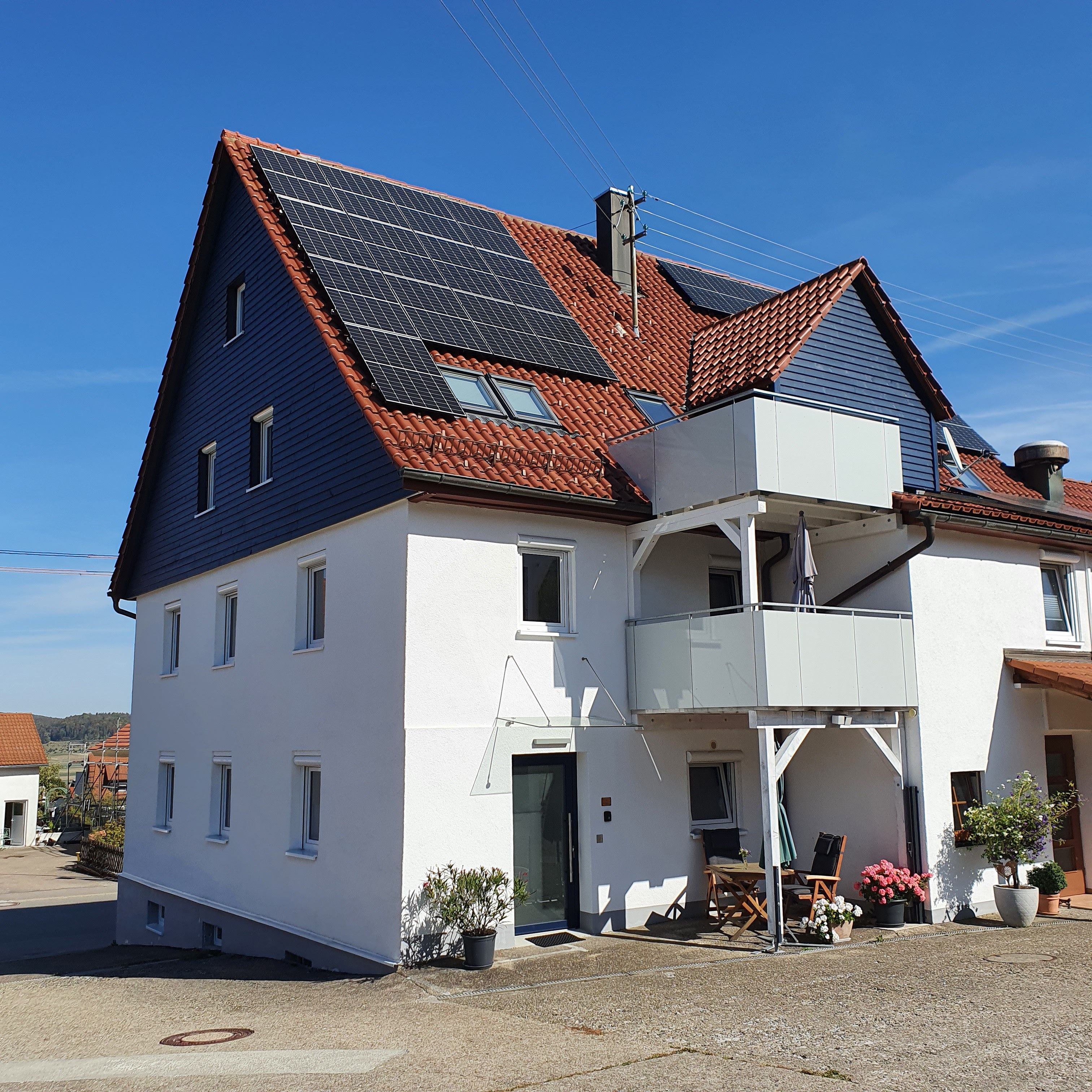 Un edificio de dos pisos con techo inclinado, paneles solares y un balcón.