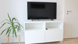 Un meuble de rangement blanc pour appareils multimédias, avec un téléviseur à écran plat, une plante en pot et une porte dotée d’une poignée.