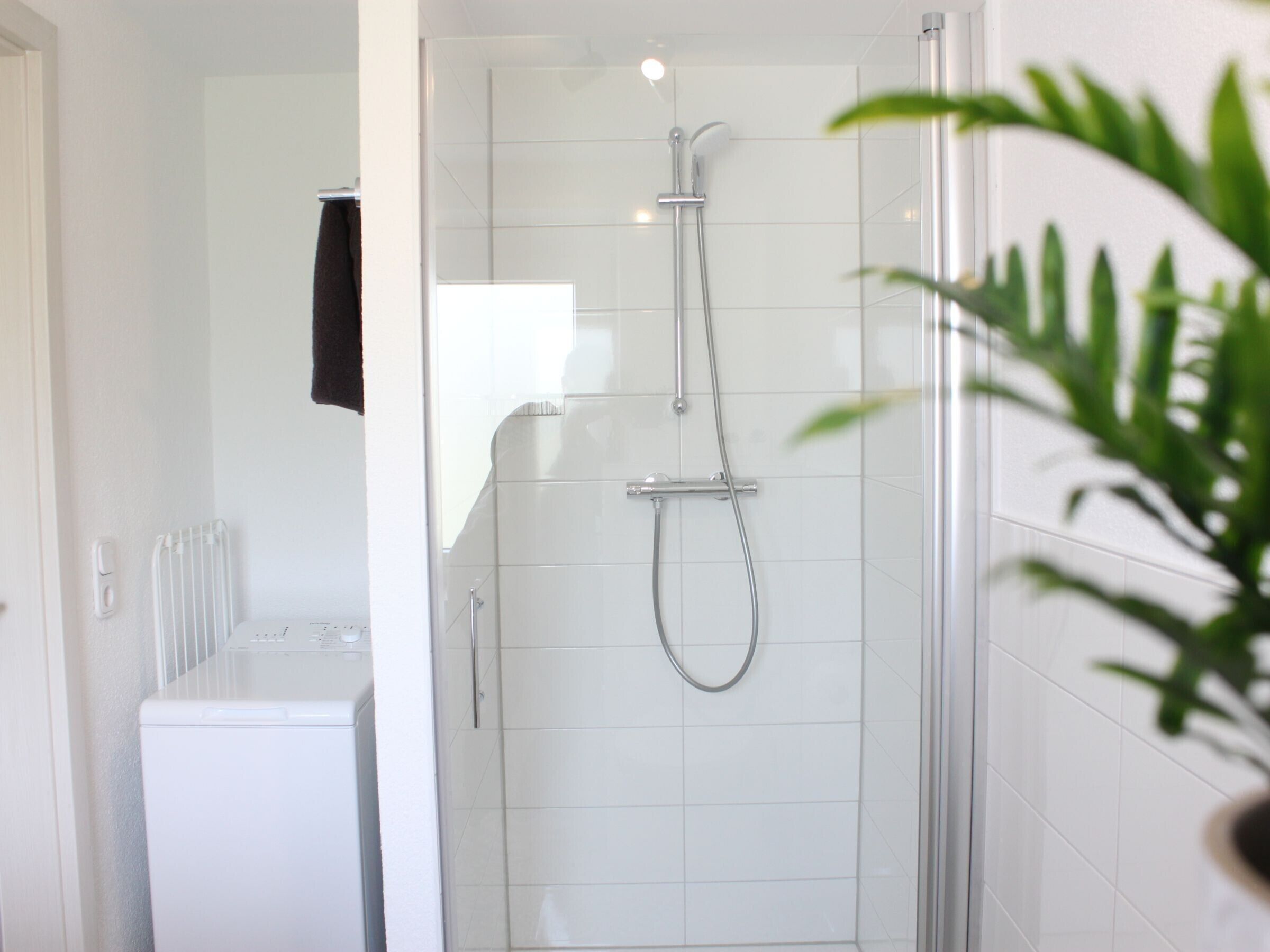 A modern bathroom with a glass-enclosed shower, a white tiled wall, and a visible washing machine.