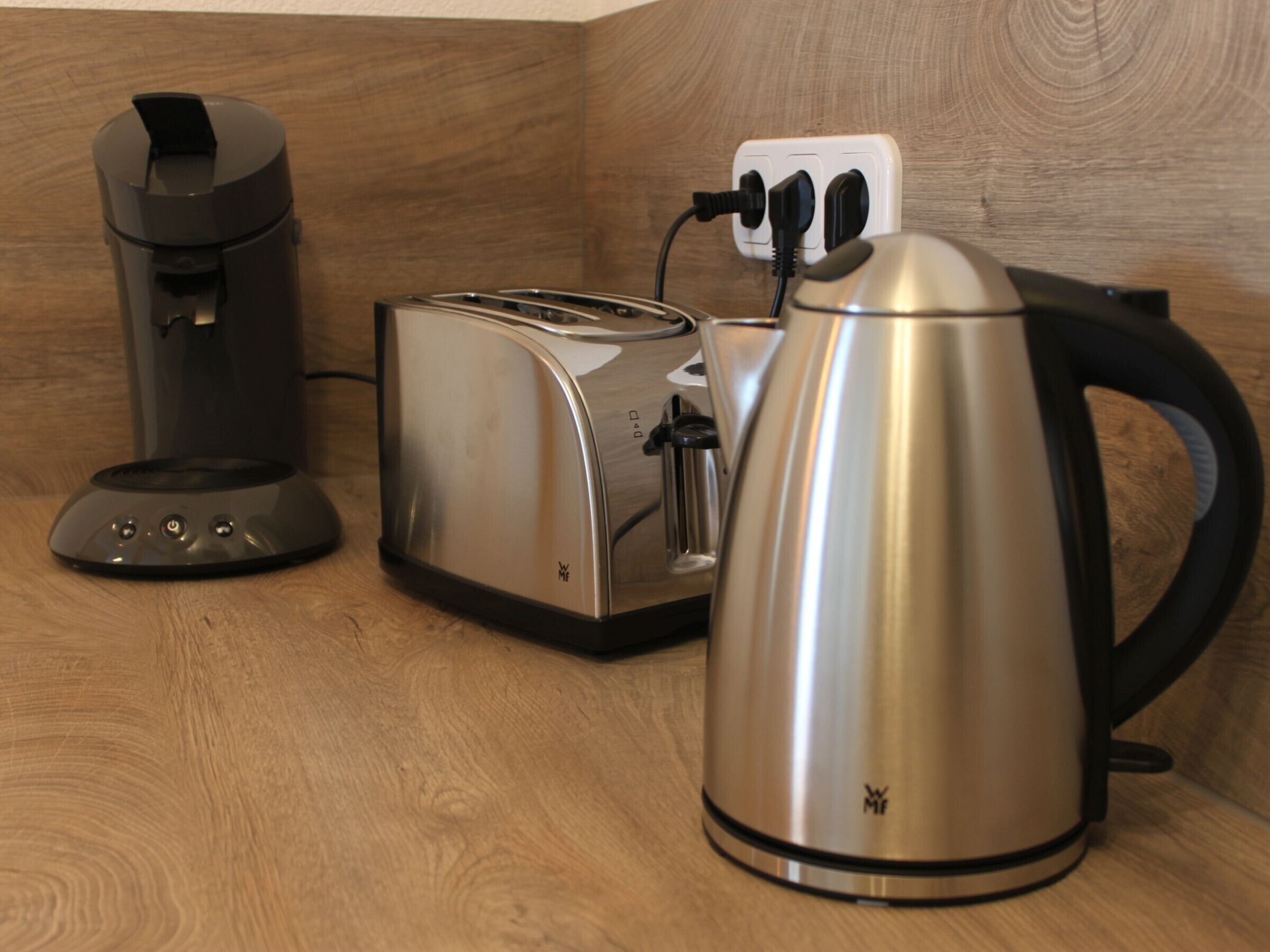 Une cuisine équipée d’une machine à café, d’un grille-pain et d’une bouilloire, le tout posé sur un plan de travail en bois.