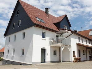 A two-story building with a red-tiled roof, a balcony with a white railing, and a small door. - Flat 2, 41 sqm, 1 bedroom with double bed, 1 sofa bed, max. 3 persons (Burladingen)