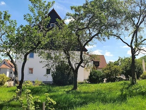 A house with a sloped roof, surrounded by lush greenery and trees. - Flat 2, 41 sqm, 1 bedroom with double bed, 1 sofa bed, max. 3 persons (Burladingen)