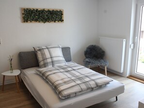 Un dormitorio con cama, una mesita de noche, una silla, un radiador y una planta sujeta a la pared.