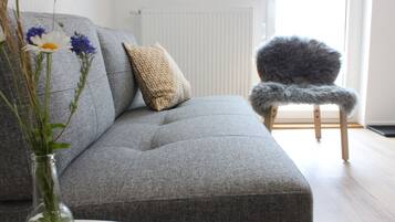 A grey sofa with a patterned pillow, a fluffy chair, and a vase with flowers.