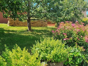 A garden with a tree, a pile of firewood, and flowering plants. - Flat 2, 41 sqm, 1 bedroom with double bed, 1 sofa bed, max. 3 persons (Burladingen)