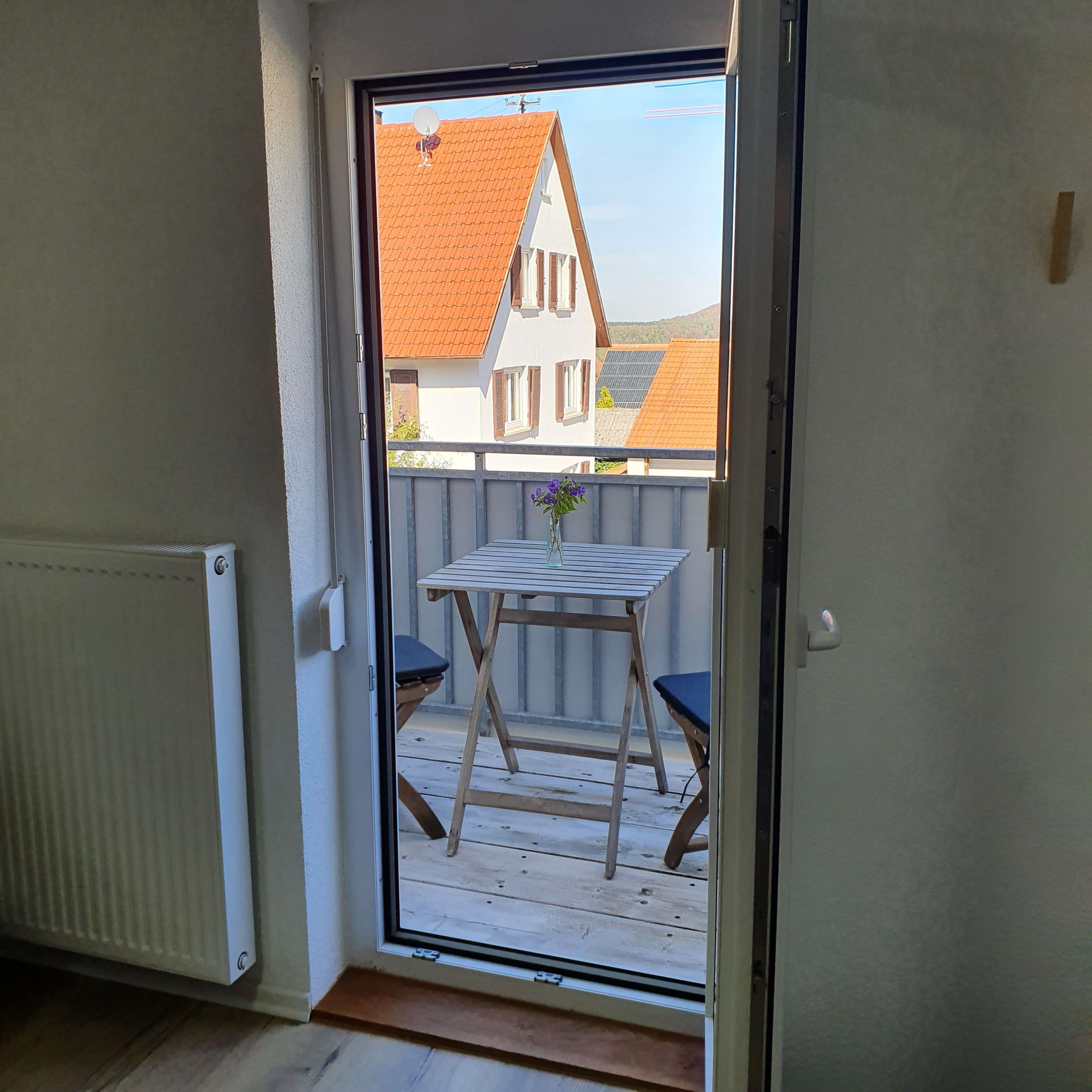 Una habitación con puerta de vidrio corredera que da a una terraza exterior con mesa y sillas.