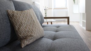 A grey sofa with a patterned pillow, a small round table, and a white radiator in the background. - Flat 3, 54 sqm, 1 bedroom with double bed and 1 sofa bed, max. 4 persons (Burladingen)