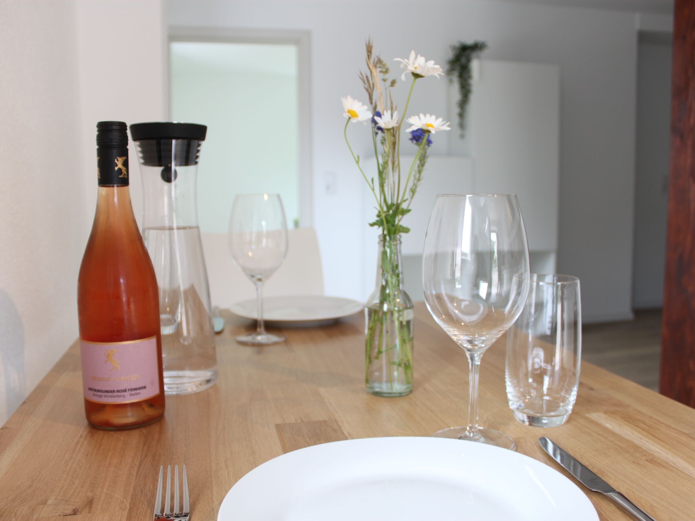 A dining table with a bottle, wine glasses, and a vase with flowers.