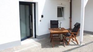 A small outdoor seating area with a table and chairs, a door, a window, and a wall-mounted light fixture. - Flat 3, 54 sqm, 1 bedroom with double bed and 1 sofa bed, max. 4 persons (Burladingen)