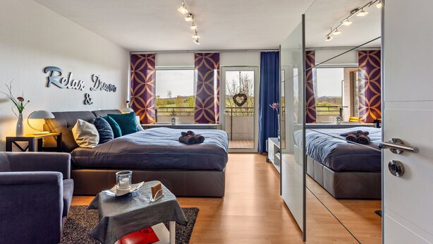 A modern bedroom with a large bed, a sofa, a small table, and a mirror. - Holiday Apartment "Comfort" with Shared Garden, Balcony & Wi-Fi (Brilon)
