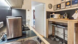 A compact kitchen with a stainless steel refrigerator, a microwave, and a sink. There are bar stools and a small bar area with bottles and glasses. - Holiday Apartment "Comfort" with Shared Garden, Balcony & Wi-Fi (Brilon)