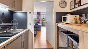 A modern kitchen with a microwave, sink, and dish rack. A hallway leads to a bedroom with a bed and a decorative wall. - Holiday Apartment "Comfort" with Shared Garden, Balcony & Wi-Fi (Brilon)