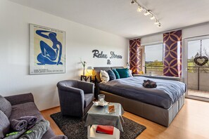A modern bedroom with a large bed, a sofa, a small table, and a wall with a poster and a 'Relax Dream' sign.