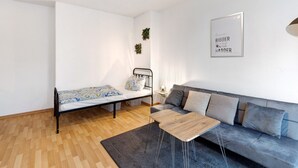 Una habitación moderna con cama, sofá, una mesita y una planta en la pared.