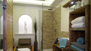 A spa room with a glass shower enclosure, a wooden bench, a statue, and a shelf with towels.