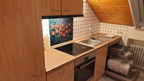 A kitchen with wooden cabinets, a black countertop, a stainless steel sink, a built-in oven, and a dish rack. - Apartment 'Fewo - Dachgeschoss' with Mountain View, Balcony and Wi-Fi (Zell am Harmersbach)