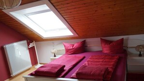 A bedroom with a skylight, a bed with pink bedding, a bedside table with a lamp, and a radiator. - Apartment 'Fewo - Dachgeschoss' with Mountain View, Balcony and Wi-Fi (Zell am Harmersbach)