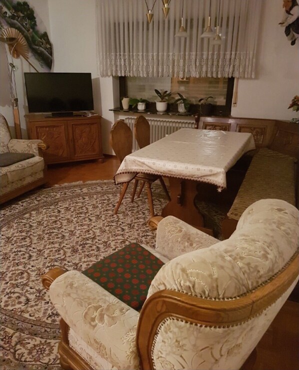 Ein Wohnzimmer mit einer Couch, einem Esstisch, einem Fernseher und einem gemusterten Teppich.