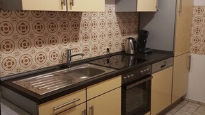 Une cuisine avec des meubles de couleur beige, un évier en acier inoxydable, une bouilloire et un four.