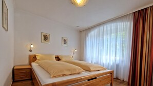 Een slaapkamer met een houten bed, twee nachtkastjes, een wandlamp en een raam met gordijnen.