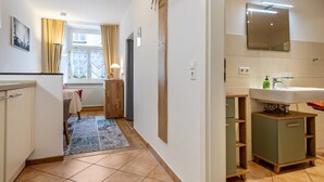 A modern kitchen with a wooden cabinet, a dining area with a table and chairs, and a bathroom with a sink and mirror.