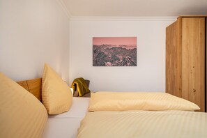 A bedroom with a bed, pillows, a wooden wardrobe, and a mountain landscape painting on the wall.