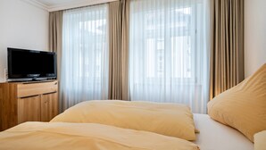 A hotel room with a bed, a TV on a wooden cabinet, and sheer curtains.