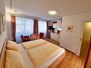 A hotel room with two beds, a dining table, a kitchen area, and a door.