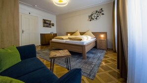A bedroom with a bed, bedside table, nightstand, a small table with a chair, a sofa, a wall-mounted light fixture, and a door. - Apartment 'Ferienwohnung S5' with Wi-Fi (Lindau am Bodensee)